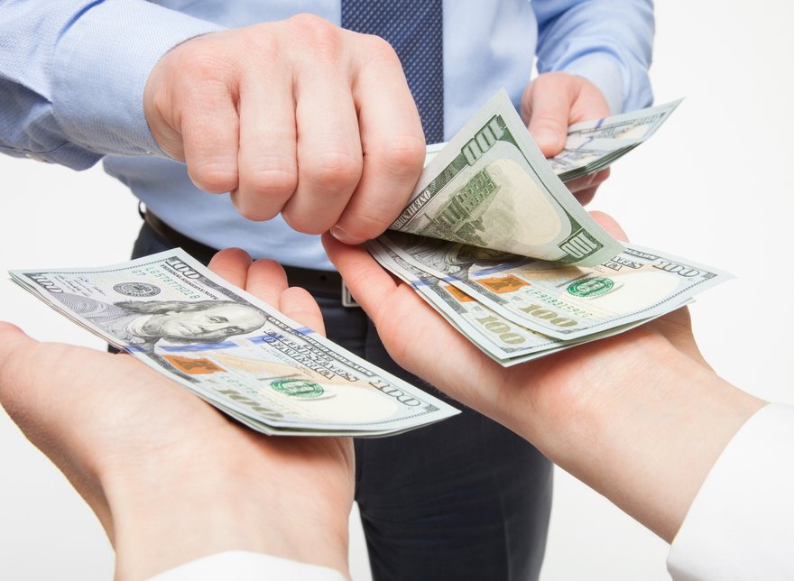 A person placing hundred dollar bills into the outstretched palms of another person.
