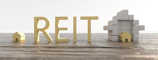 Wooden blocks spelling REIT next to real estate building blocks.