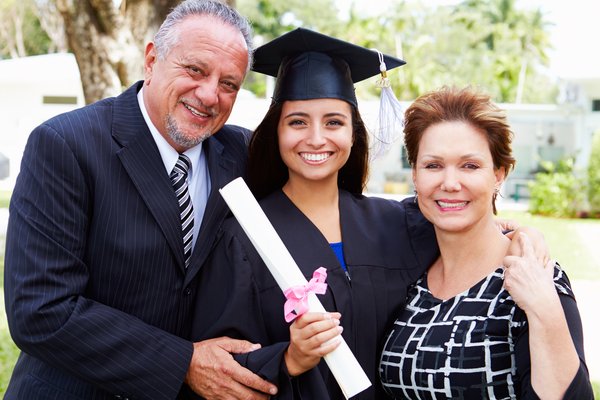 Two people standing with a graduate in cap and gown and holding their diploma.