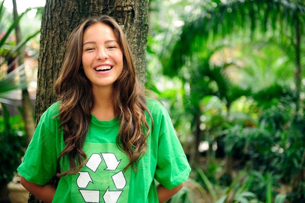 Young adult smiling and wearing a t-shirt with the recycle logo on it.