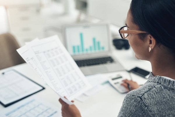 A woman looking at financial statements and typing numbers in a calculator.