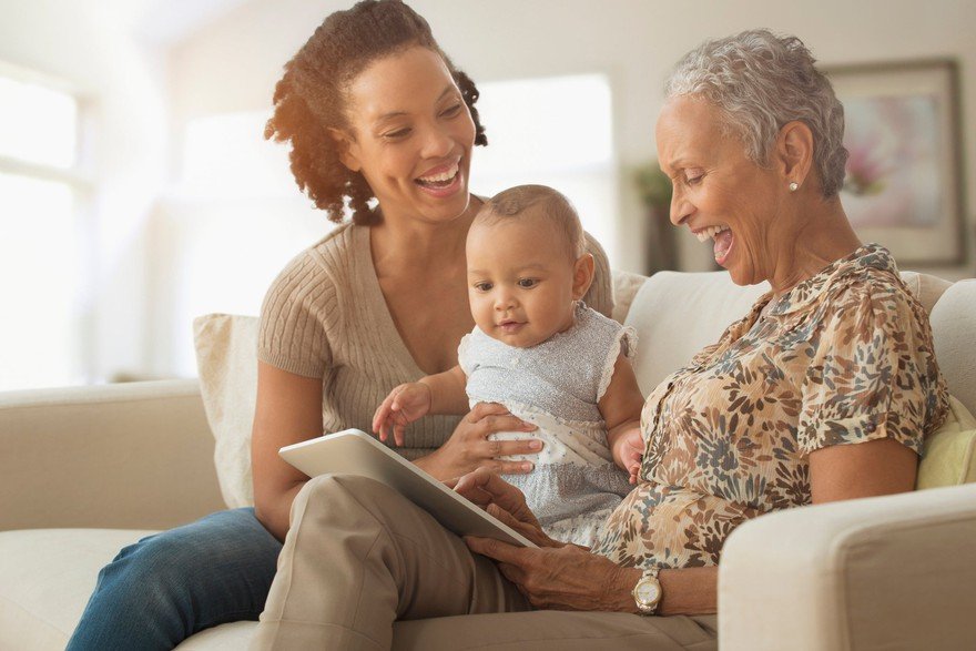 Senior laughs with adult and small child on couch at home.