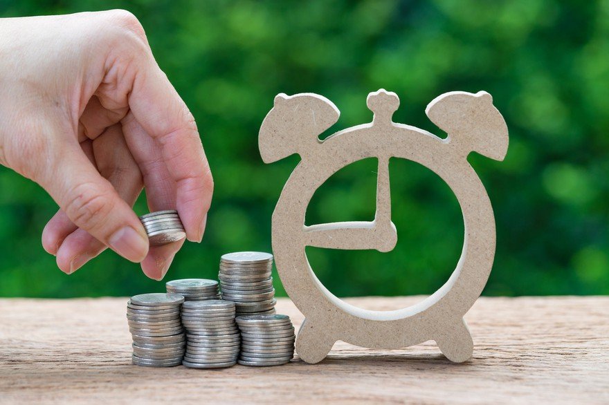 A person stacking coins next to a wood clock cutout.