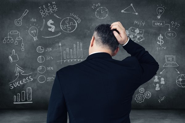 Man scratching his head as he looks at a chalkboard full of various equations.